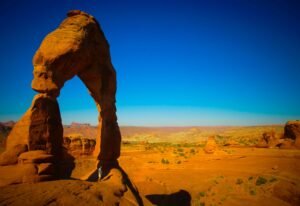Delicate Arch op een rood rotsplateau onder een heldere blauwe lucht in Arches National Park.