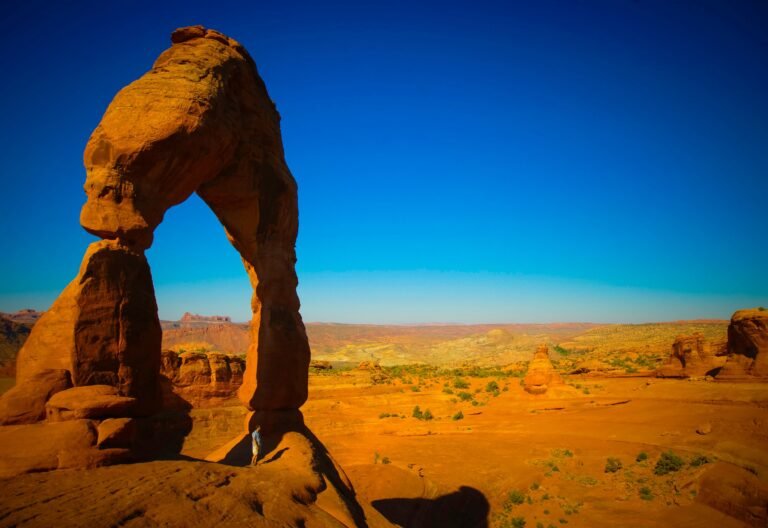 Delicate Arch op een rood rotsplateau onder een heldere blauwe lucht in Arches National Park.