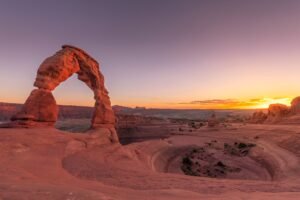 Delicate Arch op een rood rotsplateau onder een heldere blauwe lucht in Arches National Park.
