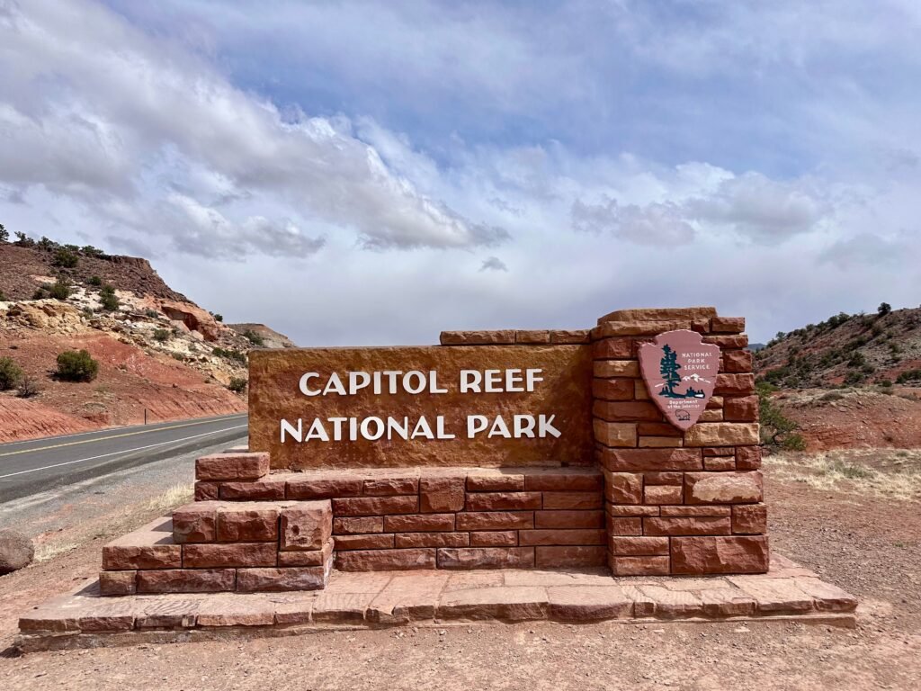 Welkomstbord van Capitol Reef National Park langs de toegangsweg, met rode rotsformaties en woestijnlandschap op de achtergrond.